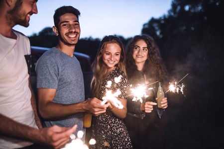 A group of friends with sparklers standing outdoors at dusk.の写真素材