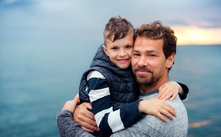 Father with small son on a walk outdoors standing on beach at dusk.の写真素材