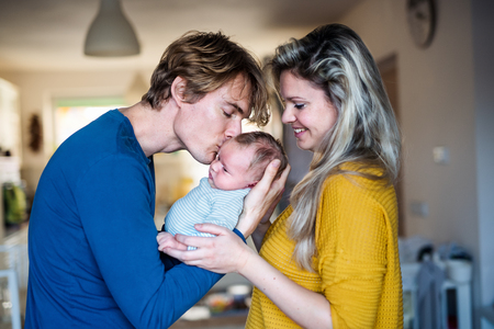 Beautiful young parents with a newborn baby at home, kissing.の写真素材