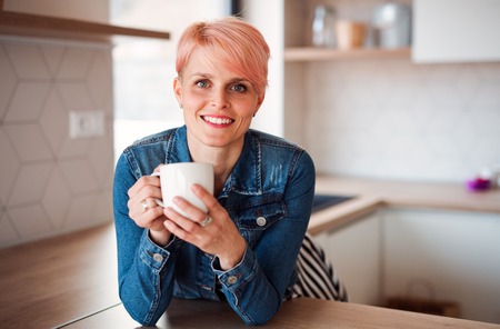 A young attractive woman leaning on a counter in a kitchen at home.の写真素材