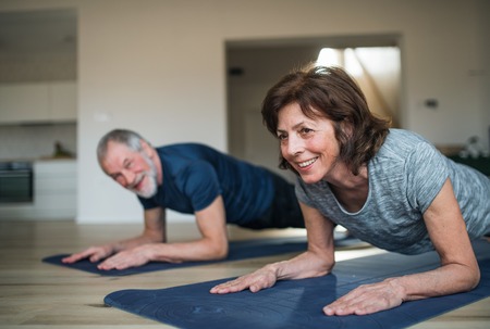 A senior couple indoors at home, doing exercise on the floor.の写真素材