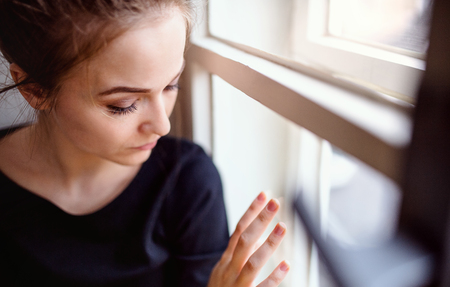 A close-up of young sad female student sitting on window sill.の写真素材