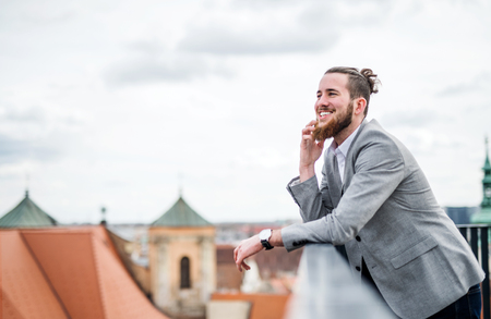 A young businessman with smartphone standing on a terrace, making a phone call.の写真素材