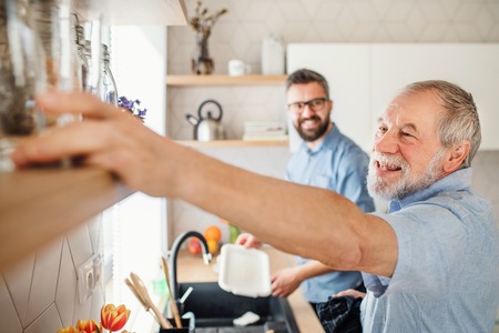 Adult hipster son and senior father indoors in kitchen at home, washing dishes.の写真素材