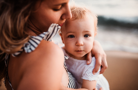Close-up of young mother with a toddler girl on beach on summer holiday.の写真素材