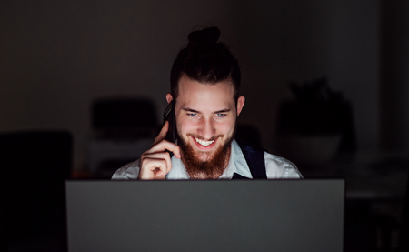 A portrait of young businessman with smartphone in an office at night, working.の写真素材