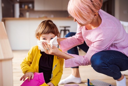 Mother blowing her small daughters nose when playing at home.の写真素材
