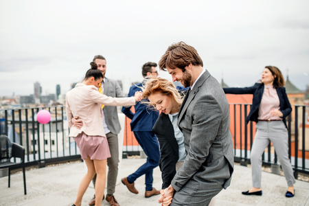 A group of joyful businesspeople having a party outdoors on roof terrace in city, dancing.の写真素材