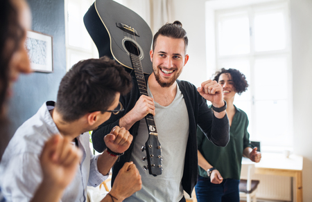 A group of young friends with guitar indoors at home, house sharing concept.の写真素材