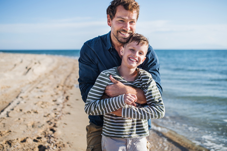 Father with small son on a walk outdoors on beach, having fun.の写真素材