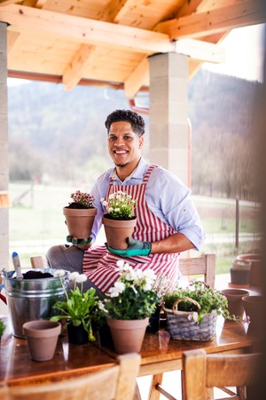 A portrait of young man gardener outdoors at home, planting flowers.