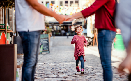 A small girl running towards unrecognizable parents outdoors in town.の写真素材