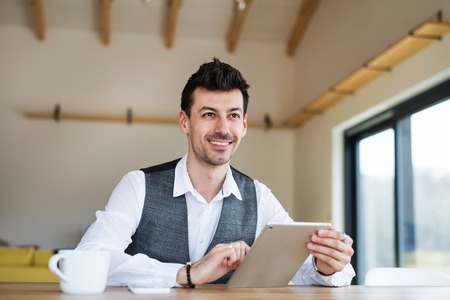 Young man with coffee sitting at the table, using tablet.の写真素材