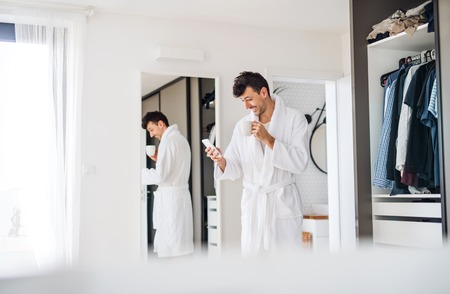 Young man with coffee and smartphone in the bedroom, a morning routine.の写真素材
