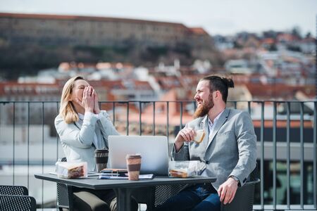 Two young business people sitting on a terrace outside office, having lunch break.の写真素材