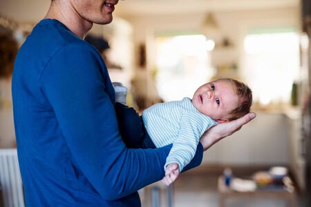 Midsection of young father holding a newborn baby at home.