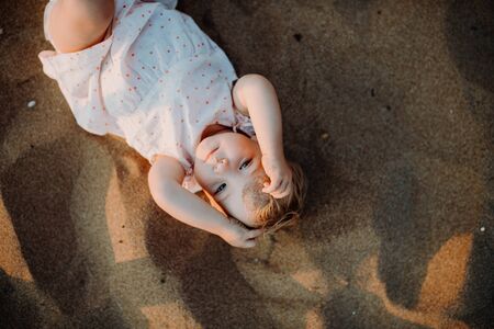 A top view of small toddler girl playing in sand on beach on summer holiday.の写真素材