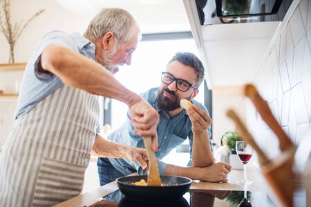 An adult hipster son and senior father indoors at home, cooking.の写真素材