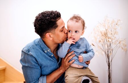 A portrait of father and small toddler son indoors at home, sitting on staircase.の写真素材