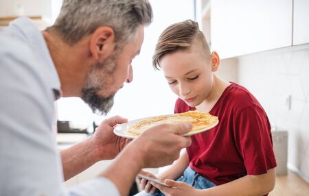 Mature father with small son indoors in kitchen, making pancakes.の写真素材