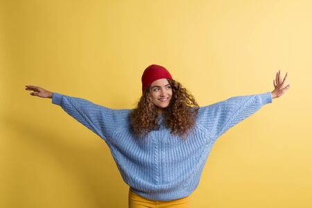 Portrait of a young woman with woolen hat in a studio on a yellow background.