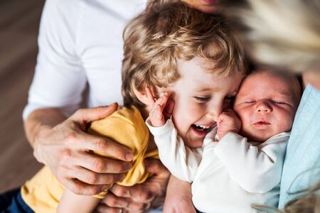 Midsection of father with newborn baby and small toddler son at home.の写真素材