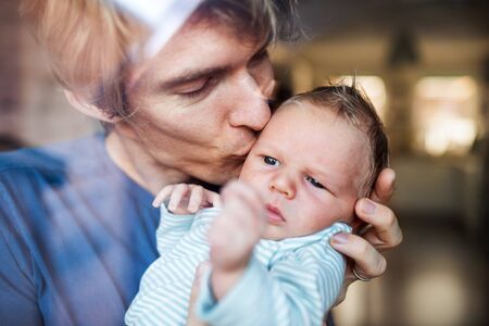A young father holding a newborn baby at home, kissing.