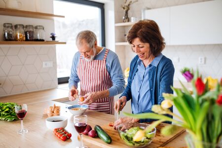 A portrait of senior couple in love indoors at home, cooking.の写真素材