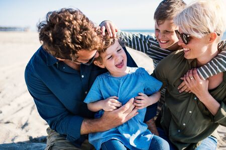 Young family with two small children sitting outdoors on beach, having fun.