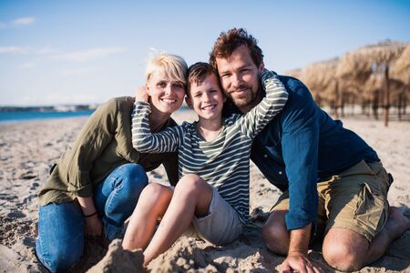 Young family with small boy sitting outdoors on beach, looking at camera.の写真素材