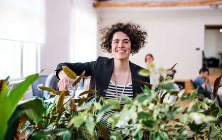 Young woman watering plants in office, start-up business.の写真素材