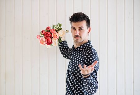 Young man with flowers standing against white wooden background wall.の写真素材