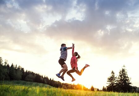 Active young couple jumping after doing exercise in nature at sunset.の写真素材