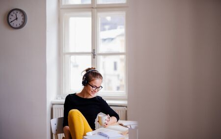 A young female student sitting at the table, using headphones when studying.