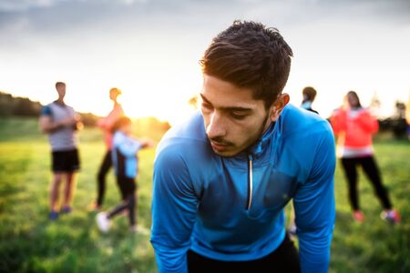 A portrait of young man with large group of people doing exercise in nature.の写真素材