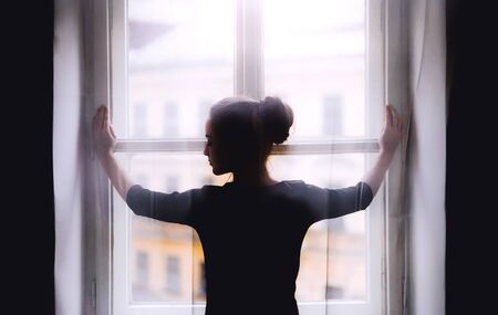 Rear view of young sad female student standing by window.の写真素材