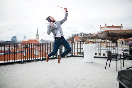 A young businessman with headphones standing on a terrace, having fun.の写真素材