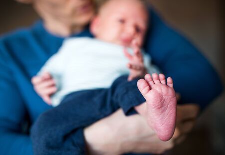 A father holding a newborn baby at home, bare foot in the foreground.