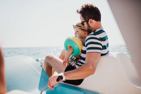 Father with small son sitting on boat on summer holiday.の写真素材