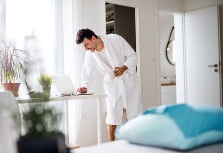 Young man with laptop and coffee in the bedroom in the morning.の写真素材