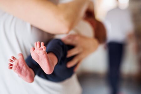 A mother holding a newborn baby at home, bare feet in the foreground.の写真素材