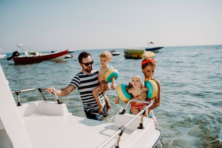 Parents with two small toddler children standing by boat on summer holiday.