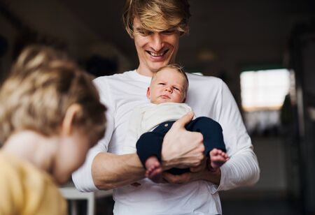 A young father with a newborn baby and toddler son at home.