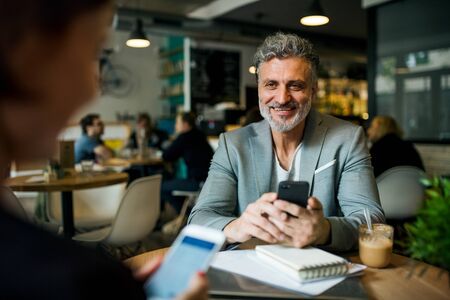 Man and woman having business meeting in a cafe, using smartphones.