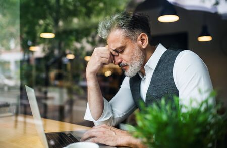 Frustrated mature man sitting at the table in a cafe, using laptop.の写真素材