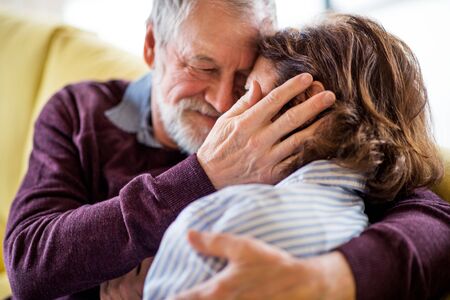 Affectionate senior couple in love sitting on sofa indoors at home, hugging.