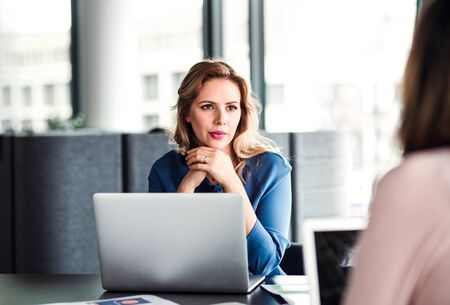 Young businesswoman with laptop sitting in an office, talking to a colleague.の写真素材