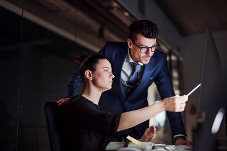 Young business people in an office at night, using computer.