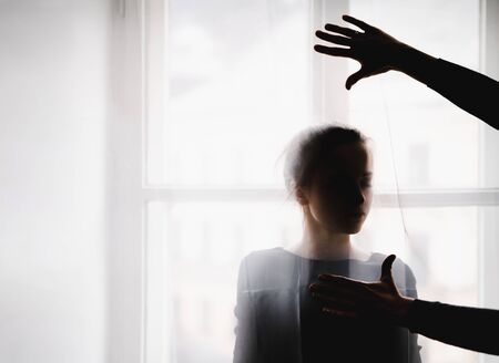A silhouette of young woman standing by window. Copy space.