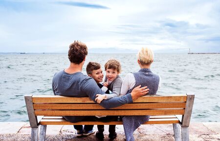 Young family with two small children sitting on bench outdoors on beach.の写真素材